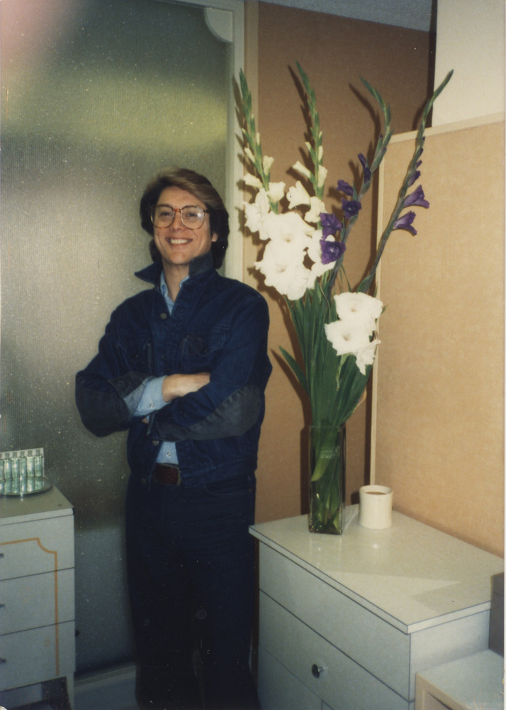 Download the full-sized image of Photograph of Person Smiling next to Vase of Flowers