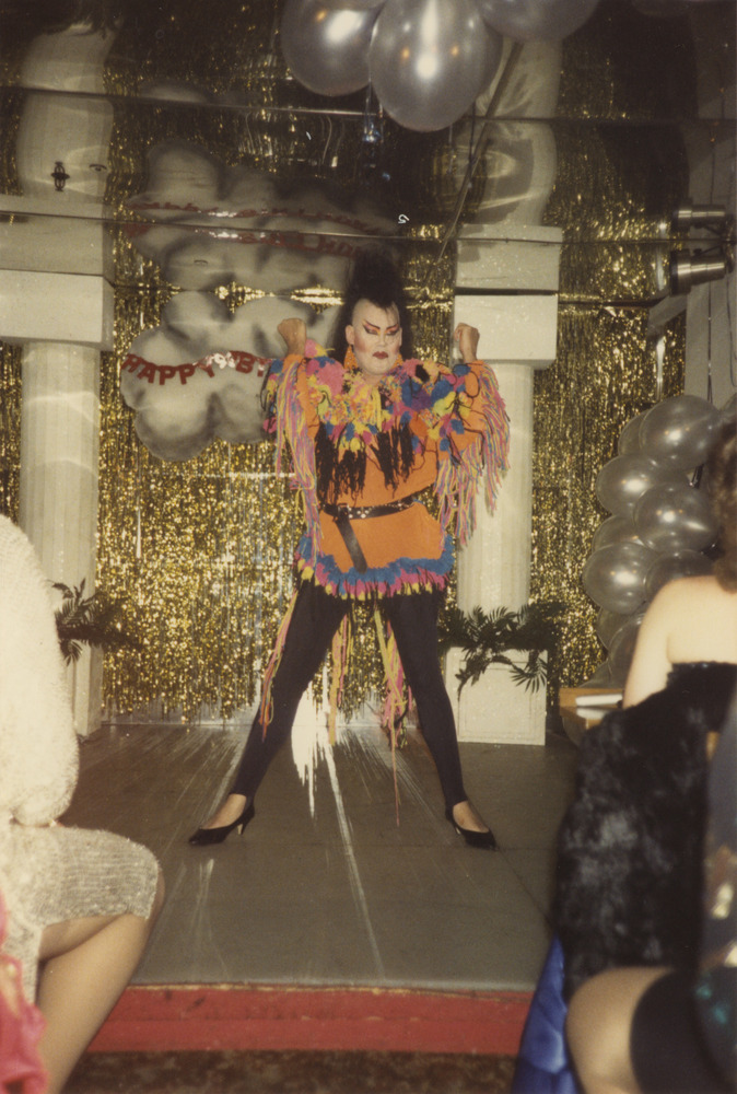 Download the full-sized image of Photograph of Person on Stage in Orange and Multicolor Top